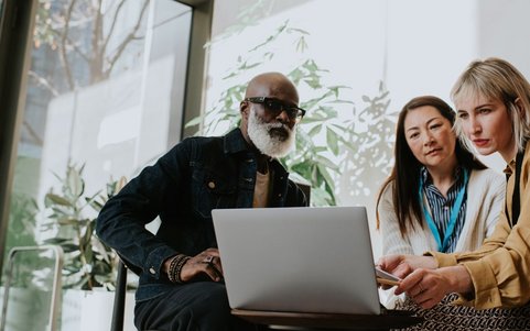 Three employees analyzing information together on a laptop.