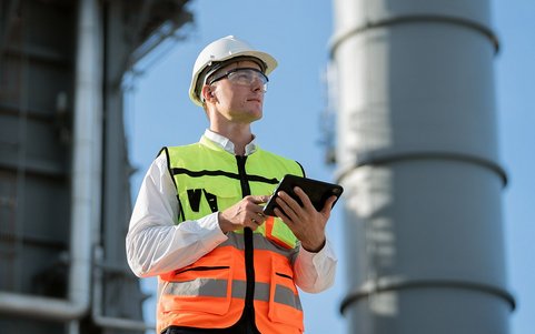 Quentic AI in action: Safety professional in high-visibility vest and hard hat using a tablet during an inspection at an industrial facility
