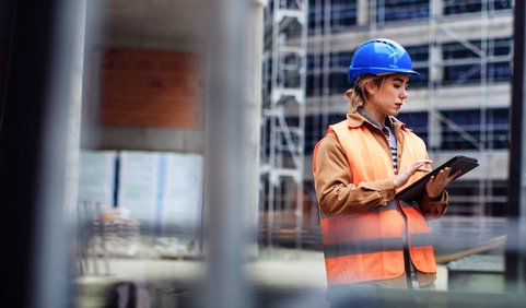 A occupational safety professional with a blue helmet, using an EHS app on a tablet